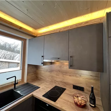 Eine moderne Küche mit Holz- und Grautönen. Es gibt einen schönen Ausblick durch das Fenster und eine elegante Beleuchtung.