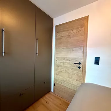 Ein modernes Schlafzimmer mit einem Holzschrank und einer hellen Holztür. Der Boden ist aus Holz und die Wände sind neutral gehalten.