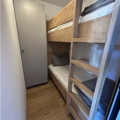Ein kleines Zimmer mit einem Etagenbett aus Holz. Die Wände sind hell und der Boden ist aus Holz.