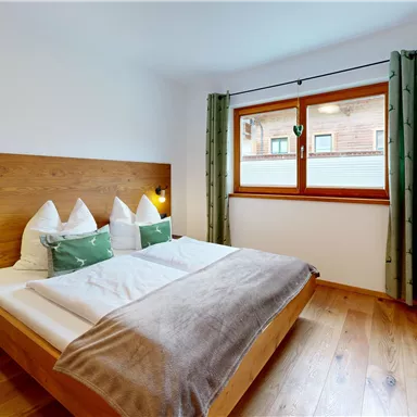A cozy bedroom with a double bed and wooden details. Large windows provide plenty of daylight.