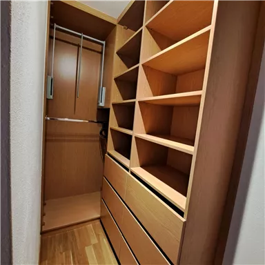 Ein gut organisierter Kleiderschrank aus Holz mit Regalen und Schubladen. Die Inneneinrichtung ist hell und modern.