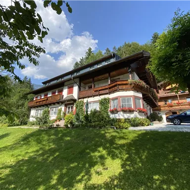 Ein charmantes Haus in einer grünen Umgebung mit gemütlichen Balkonen. Die Sonne scheint und der Himmel ist teilweise bewölkt.