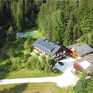 Ein malerisches Anwesen umgeben von dichten Wäldern. Die Gebäude liegen in einer ruhigen, grünen Landschaft mit einem asphaltierten Weg.