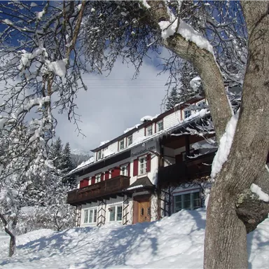 Ein charmantes Haus im Schnee, umgeben von schneebedeckten Bäumen. Der Himmel ist klar und blau.