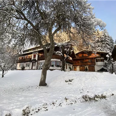 Ein malerisches chaletähnliches Gebäude im Schnee umgeben von verschneiten Bäumen. Der klare Himmel und die verschneite Landschaft schaffen eine gemütliche Winteratmosphäre.