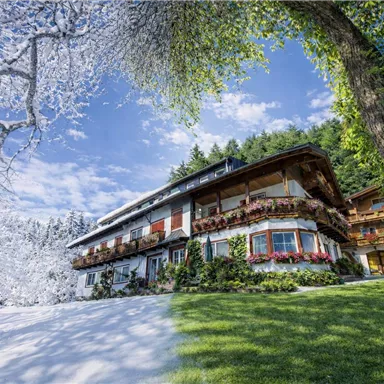Ein malerisches Gebäude inmitten einer winterlichen Landschaft. Schnee bedeckt den Boden, während die Fassade mit bunten Blumen geschmückt ist.