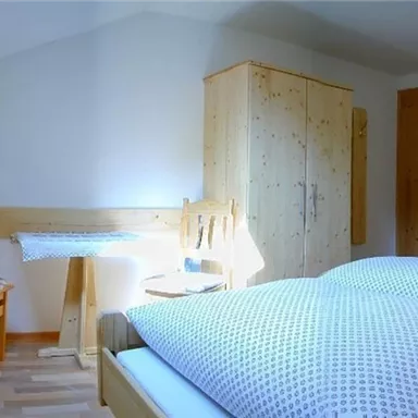 Ein gemütliches Schlafzimmer mit einem Doppelbett und einem Schreibtisch. Die Wände sind hell und es gibt Holzdetails, die eine warme Atmosphäre schaffen.
