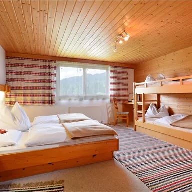 A cozy room with wood paneling, a double bed, and a bunk bed. Large windows provide a view of the surroundings and ensure plenty of daylight.
