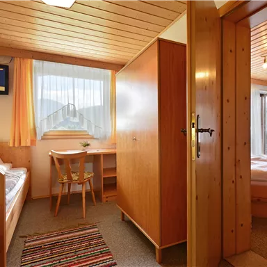 A cozy room with wooden furniture and a television. The large window lets in plenty of light and offers a view outside.