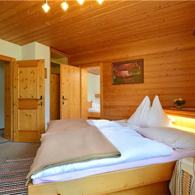 A cozy bedroom with wooden paneling. There is a large bed, a chair, and nice decoration.