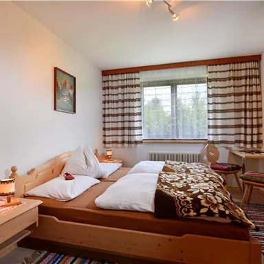 A cozy bedroom with a double bed and a television. The windows let in plenty of light, and there is stylish wood decor.