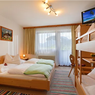 A cozy room with two beds and a loft bed. A television and large windows create a bright atmosphere.