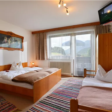 A cozy room with a double bed and a single bed.  
Large windows offer a view of the mountains and there are wooden furniture as well as a television.