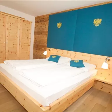 A modern bedroom with a large double bed and wooden paneling. The walls are in calming colors, and there is a spacious wardrobe.