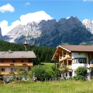 Ein malerisches Bergdorf mit traditionellen Häusern und majestätischen Bergen im Hintergrund. Der Himmel ist klar und die Landschaft ist üppig und grün.
