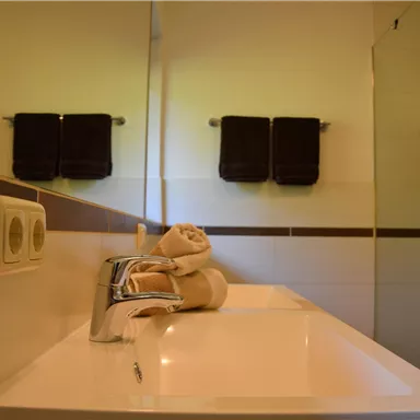A modern bathroom with a sink and towels. The shower is separated by a glass wall.