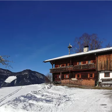 Ein gemütliches Holzhaus im Schnee, umgeben von Bergen. Der klare blaue Himmel sorgt für eine schöne Winteratmosphäre.