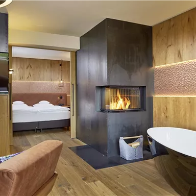 A modern room with an open fireplace and a freestanding bathtub. Warm wood and cozy furniture create an inviting atmosphere.