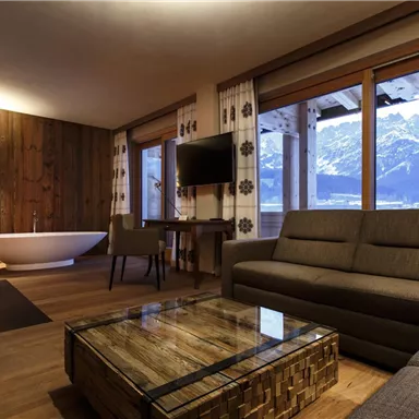 A modern living room with a cozy sofa and a wooden table. Large windows offer a view of the mountains and let in plenty of daylight.