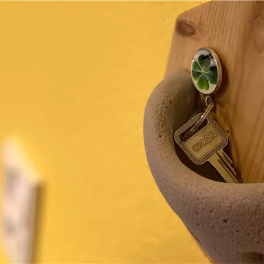 A key hangs on a wooden holder on a yellow wall. The scene depicts a simple and inviting setup.