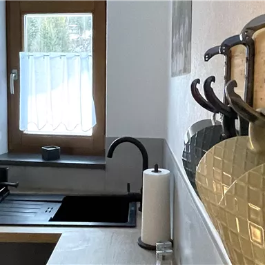 A modern kitchen with an elegant sink and wooden shelves. Practical kitchen utensils hang on the wall.