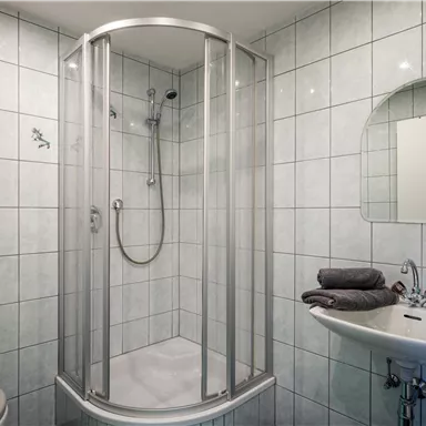A modern bathroom with a glass shower and white tiles. Towels in blue and gray are lying on the sink.