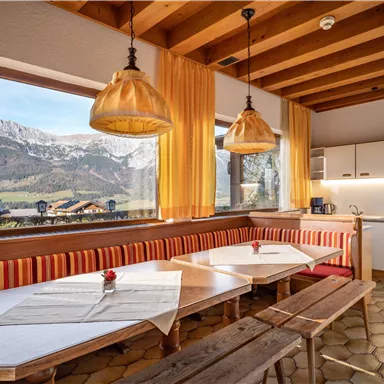 A cozy dining area with a large table and wooden benches. Through the windows, you can see the snow-covered mountains and the beautiful landscape.