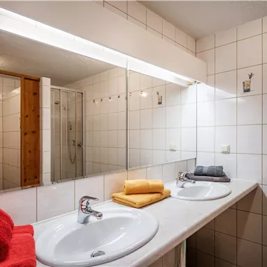 A bright bathroom with two sinks and large mirrors. Colorful towels in red and yellow are neatly arranged.
