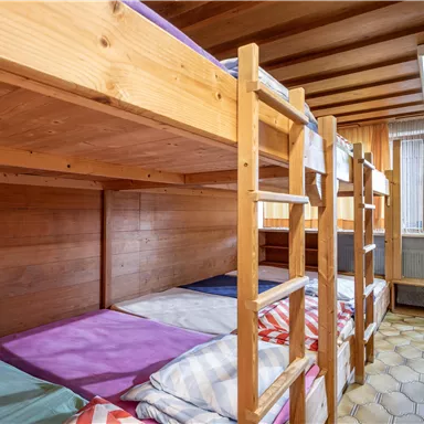 A dormitory with two wooden bunk beds. The room has a bright wood look and a window that lets in daylight.
