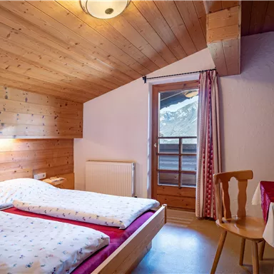 A cozy bedroom with wood paneling and two beds. The room has a window with a view of the mountains and a small table.