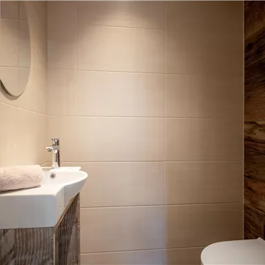 A modern bathroom with a sink and a mirror. The walls are accented with light tiles and wood.