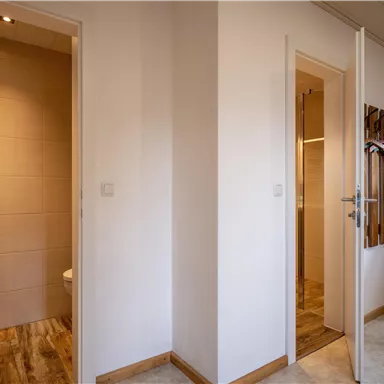 A bright corridor with two doors leading to a bathroom and another room. The floor is wooden and the walls are painted in neutral colors.