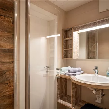 A modern bathroom with a shower and a sink. Wooden panels and tidy towels create a cozy atmosphere.