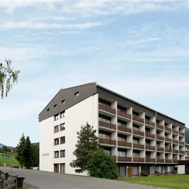 Ein modernes Gebäude mit mehreren Etagen in einer ländlichen Umgebung. Umgeben von Bäumen und sanften Hügeln bietet es eine ruhige Atmosphäre.