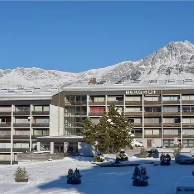 Ein modernes Hotelgebäude im Schnee, umgeben von Bergen. Die Landschaft ist klar und sonnig, mit einer friedlichen Atmosphäre.