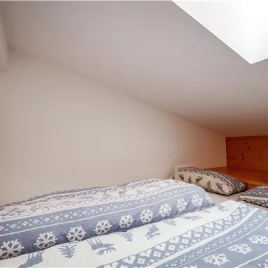 Ein gemütliches Schlafzimmer mit Holzwänden und Dachschräge. Die Bettwäsche hat ein hübsches, blau-weißes Muster.