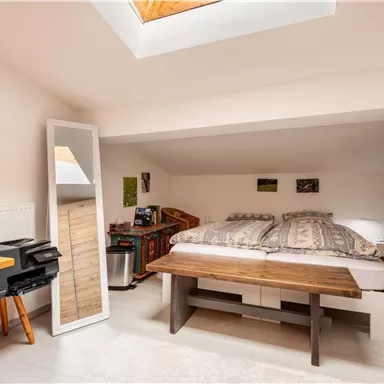 Ein gemütliches Schlafzimmer mit einem großen Bett und einer Holzkommode. Es hat Fenster und einen Schreibtisch mit Stuhl.