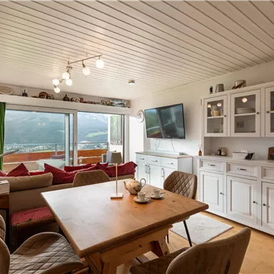 Eine gemütliche Küche mit einem Holztisch und modernen Möbeln. Große Fenster bieten einen schönen Ausblick auf die Landschaft.