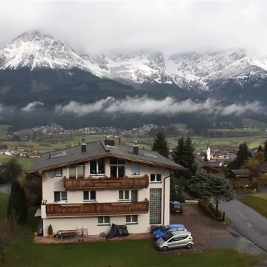 Ein modernes Haus in der Nähe einer malerischen Berglandschaft. Die schneebedeckten Berge und das grüne Tal schaffen eine beeindruckende Kulisse.