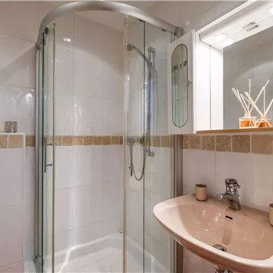A modern bathroom with a glass shower and an elegant sink. Subtle decorations and bright tiles create an inviting atmosphere.