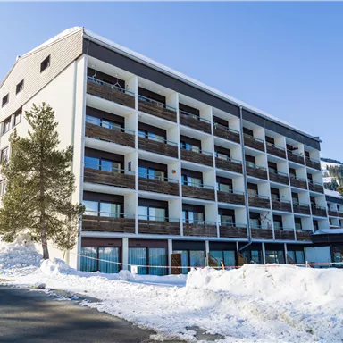 A modern hotel building in a snow-covered winter landscape. The balconies are visible, and the surroundings are quiet and inviting.