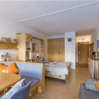 A cozy room with wooden decorations and modern furnishings. There is a dining area, a bed, and a television that displays beautiful mountain views.