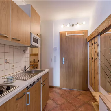 A small kitchen with wooden cabinets and modern appliances. The entrance area has a mirror and a coat rack.