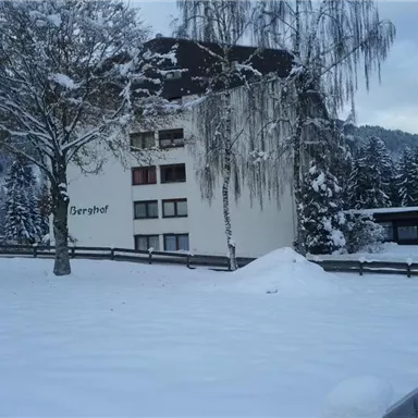 A snow-covered building with the inscription "Berghof". In the background, snow-covered trees and hills are visible.