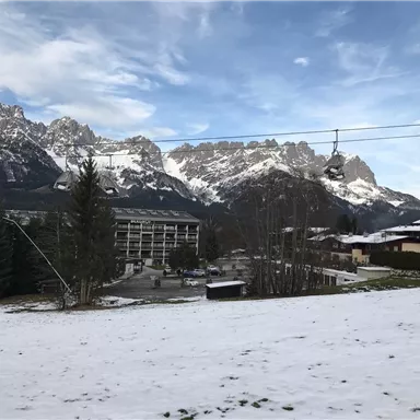 A snow-covered landscape with impressive mountains in the background. In the foreground, there is a building and a cable car.