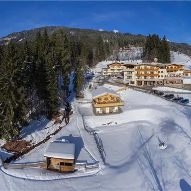A picturesque winter landscape with snow-covered mountains and a tranquil river. In the foreground, there is a charming hotel surrounded by trees.