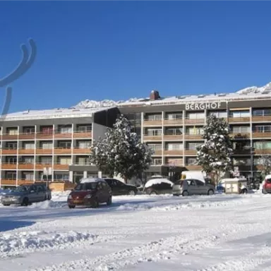 A hotel building in the snow with the inscription "Berghof". Surrounded by snow-covered trees and a clear blue sky.