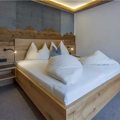 A modern bedroom with a wooden bed and cozy white pillows. The soft lighting creates a relaxed atmosphere.