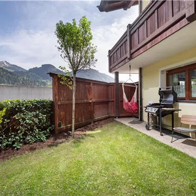 Ein gemütlicher Garten mit einem Grill und Sitzgelegenheiten. Im Hintergrund sind Berge zu sehen und der Himmel ist klar.