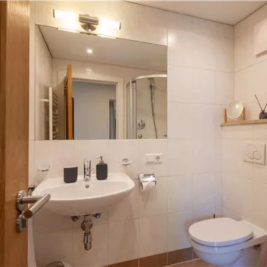 Ein modernes Badezimmer mit einem Waschbecken, einem Spiegel und einer Dusche. Es ist hell und sauber, mit einer minimalistischen Einrichtung.